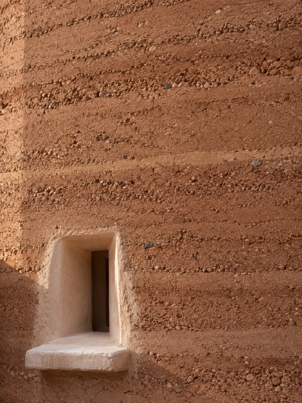 Close-up of the rammed-earth wall, its layers and small stones in raking light